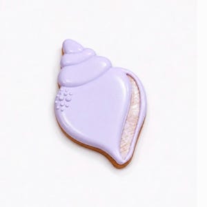 May include: A seashell-shaped cookie with a light purple glaze. The cookie has a brown, baked edge and a textured, light pink interior. Small, round details are visible on the left side of the shell.