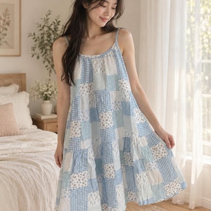 May include: A knee-length sleeveless dress featuring a patchwork design of light blue and white fabrics. The pattern alternates between blue and white gingham checks and a small floral print on a white background, with a tiered skirt silhouette.