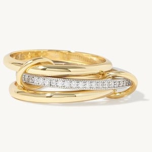 Peut inclure: Une bague en or composée de trois anneaux entrelacés. Deux des anneaux sont en or jaune lisse et poli, tandis que l'anneau central est de couleur argentée et incrusté d'une rangée de petites pierres claires et scintillantes.