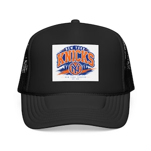 Puede incluir: Una gorra tipo camionero negra con un parche rectangular blanco en la parte frontal. El parche muestra el logotipo naranja y azul de los New York Knicks con el texto NEW YORK KNICKS, NEW YORK FOREVER y EST. 1946, sobre un horizonte urbano.