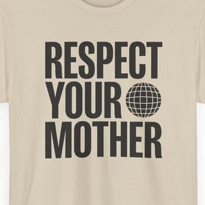 Può includere: Una t-shirt beige a maniche corte con la scritta nera "RESPECT YOUR MOTHER" stampata sul davanti, in cui un globo sostituisce la lettera "O" nella parola "YOUR". Il capo presenta uno scollo rotondo e un orlo dritto.