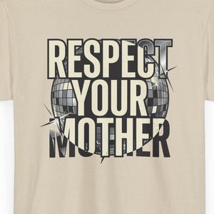 Può includere: Una t-shirt beige a maniche corte con la grafica di una palla da discoteca e il testo "RESPECT YOUR MOTHER" stampato in grassetto nero al centro. Il design include accenti a forma di stella attorno alla grafica della palla da discoteca.
