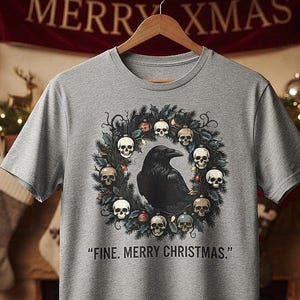 May include: A heather gray short-sleeve t-shirt featuring a graphic of a black raven centered within a holiday wreath adorned with small skulls and ornaments. Below the graphic, the text reads, "FINE. MERRY CHRISTMAS." in black capital letters.