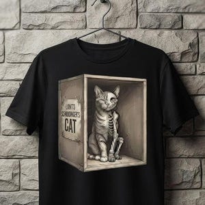 Op de afbeelding: Een zwart t-shirt met een grafische print van een kat in een houten kist. De kat is afgebeeld met aan de ene kant vacht en aan de andere kant een skelet. De kist heeft een label met de tekst "LINTS SCHRODINGER'S CAT" in zwarte letters.