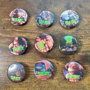 May include: A collection of eight circular pin-back buttons featuring various scenes and characters from the Teenage Mutant Ninja Turtles movie. Each button displays colorful imagery of the turtles and the text Teenage Mutant Ninja Turtles The Movie.
