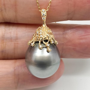 May include: A pendant necklace featuring a large, smooth, round grey pearl suspended from a textured gold cap adorned with small, clear, sparkling stones. The gold cap has an organic, branch-like design that extends downward over the pearl.