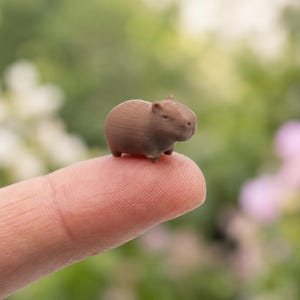 以下が含まれることがあります： 滑らかで丸みを帯びた体と小さな耳を持つ、茶色のカピバラのミニチュアフィギュア。この小さな動物の彫刻は単一の茶色で表現されており、カピバラの特徴的な顔立ちを強調するシンプルでコンパクトな形状をしています。