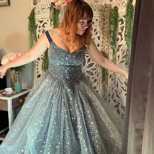 Op de afbeelding: Een donkerblauwe galajurk met een sweetheart-halslijn en een zwierige rok. De jurk is versierd met een patroon van sprankelende witte sterren. De jurk is geschikt voor speciale gelegenheden, zoals een gala of een bruiloft.