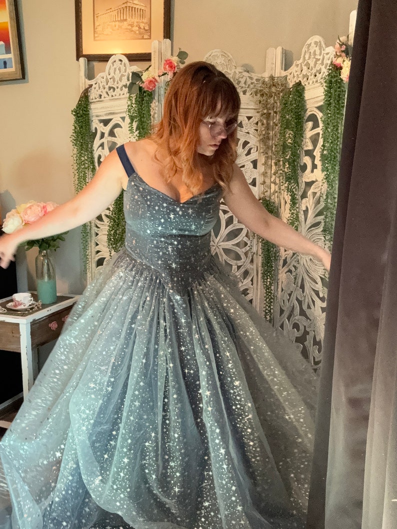 Op de afbeelding: Een donkerblauwe galajurk met een sweetheart-halslijn en een zwierige rok. De jurk is versierd met een patroon van sprankelende witte sterren. De jurk is geschikt voor speciale gelegenheden, zoals een gala of een bruiloft.