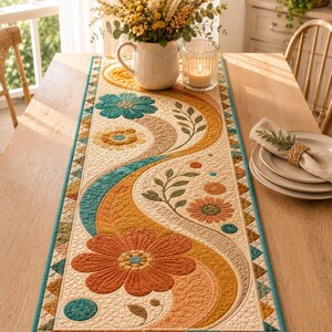 May include: A quilted table runner featuring a cream background with a flowing, wave-like pattern in shades of orange, mustard yellow, and teal. The design includes large floral motifs, leafy stems, and a geometric triangle border in teal.