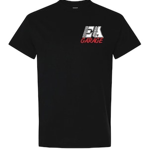 May include: A black short-sleeve t-shirt featuring a graphic on the upper left chest. The graphic displays the letters EA in white with a black outline, with the words EVERYTHING AUTO written vertically inside the letters, and the word GARAGE in red.