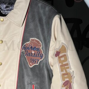 May include: A cream, black, and red leather varsity jacket with embroidered patches. The jacket features the text "Avirex Varsity 1957" and "Dokata Football Assn."