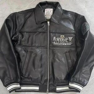 Peut inclure: Veste en cuir noir avec fermeture &eacute;clair, col et poignets et ourlet ray&eacute;s blancs. La veste porte le nom de la marque "AVIREX" en lettres argent&eacute;es avec une couronne au-dessus. Un &eacute;cusson avec le chiffre "5" est sur la manche.