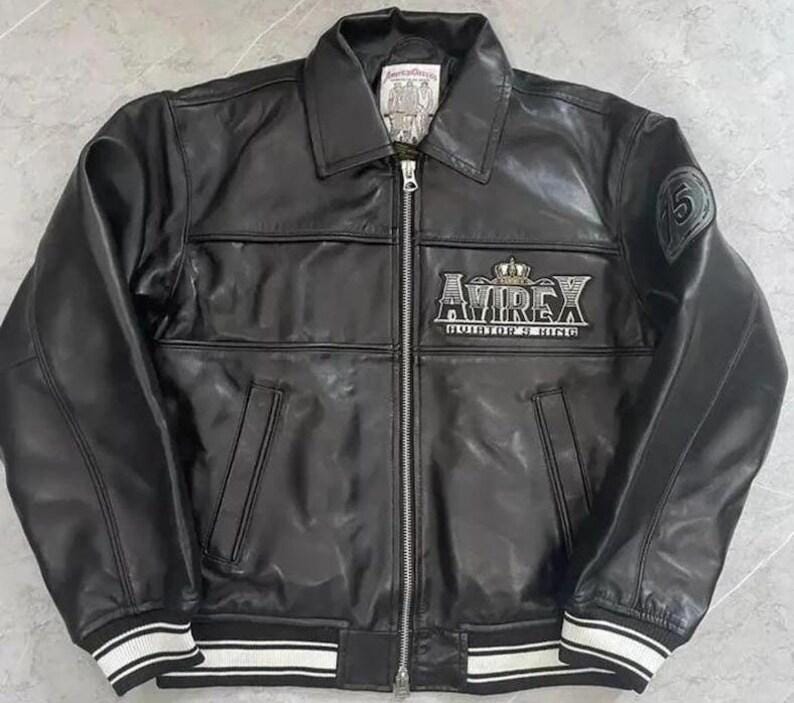 Peut inclure: Veste en cuir noir avec fermeture &eacute;clair, col et poignets et ourlet ray&eacute;s blancs. La veste porte le nom de la marque "AVIREX" en lettres argent&eacute;es avec une couronne au-dessus. Un &eacute;cusson avec le chiffre "5" est sur la manche.