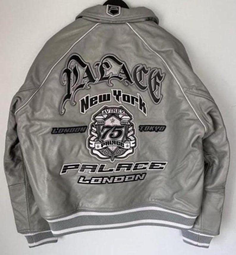 May include: Gray leather jacket with white trim and embroidered logos. The back features the word "PALACE" in large, stylized lettering, along with "New York", "London", and "Tokyo". A patch reads "75 PALACE".