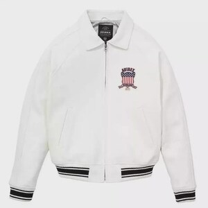 Puede incluir: Chaqueta bomber blanca con cuello y cierre de cremallera. La chaqueta presenta pu&ntilde;os y dobladillo a rayas blancas y negras. Un emblema con el texto "AVIREX" y un dise&ntilde;o de bandera americana est&aacute; en el pecho.