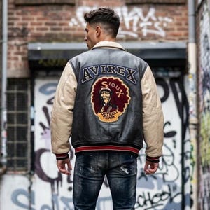 May include: Black leather jacket with beige sleeves and a cream collar. The back displays an "AVIREX" patch above a Sioux football team logo. Red and black striped trim at the waist and cuffs.
