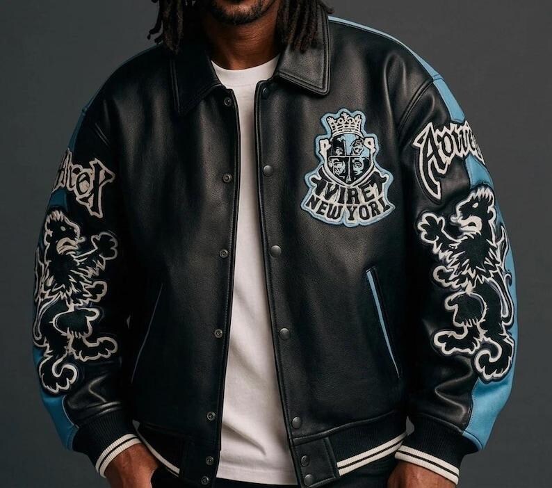 Puede incluir: Chaqueta de cuero negra con detalles en azul claro en las mangas. Cuenta con parches bordados con un le&oacute;n y el texto "AVIRE NEW YORK". La chaqueta tiene cierre de botones y cuello cl&aacute;sico.