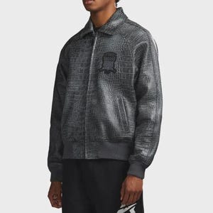 Pode incluir: Casaco bomber cinzento com textura de pele de crocodilo. O casaco tem gola, fecho de correr e um pequeno emblema no peito. Os punhos e a cintura s&atilde;o canelados. O casaco &eacute; usado com cal&ccedil;as pretas.
