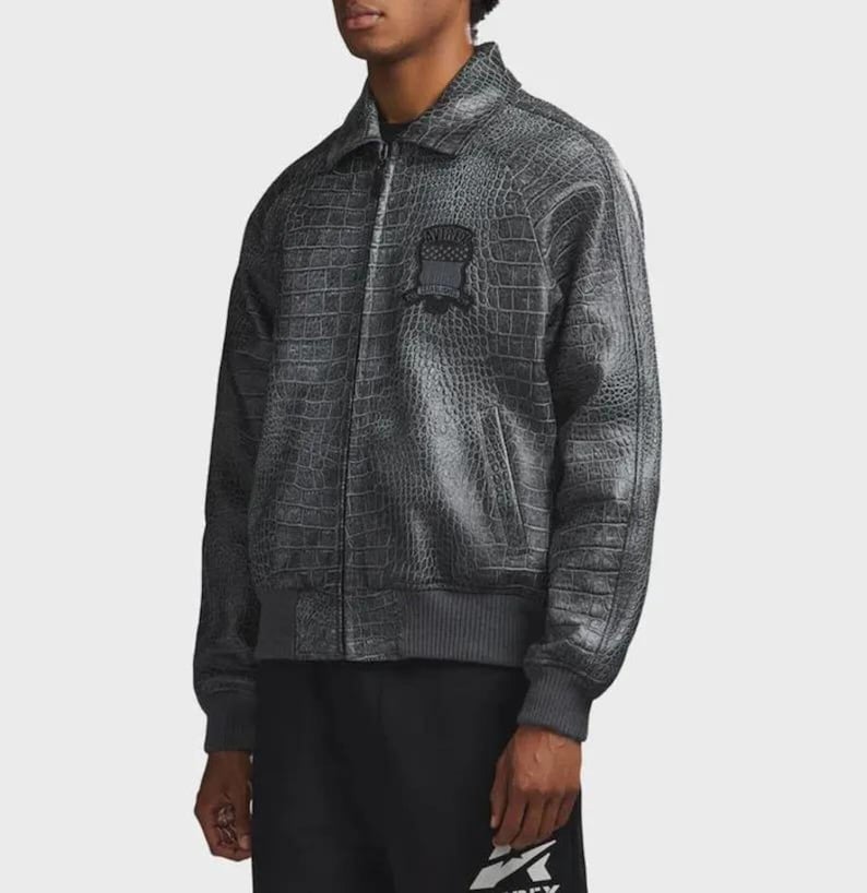 Pode incluir: Casaco bomber cinzento com textura de pele de crocodilo. O casaco tem gola, fecho de correr e um pequeno emblema no peito. Os punhos e a cintura s&atilde;o canelados. O casaco &eacute; usado com cal&ccedil;as pretas.