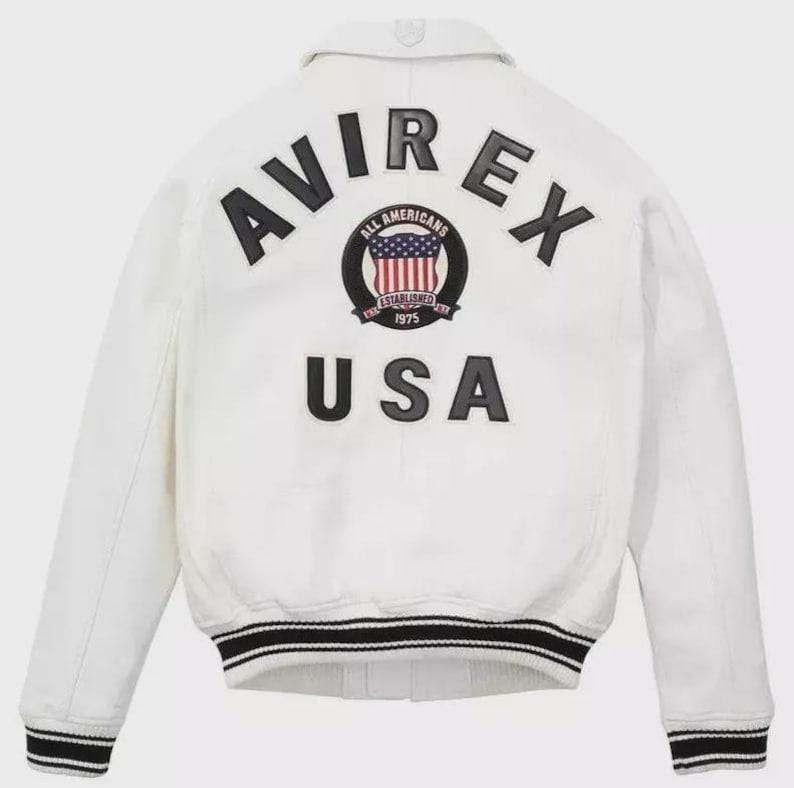 Puede incluir: Chaqueta bomber blanca con ribete a rayas blancas y negras. La parte trasera presenta el texto "AVIREX" sobre un emblema circular y la palabra "USA". El emblema incluye el texto "ALL AMERICANS ESTABLISHED 1975".