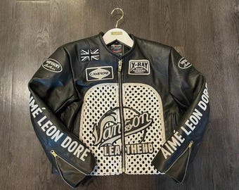 May include: Black leather jacket with white accents and patches. Features the text "Vanson Leathers" and "Aimé Leon Dore". Includes a Union Jack patch and a perforated white panel on the front. Zippers on the sleeves.