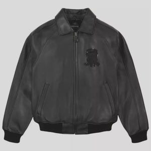 May include: Black leather bomber jacket with a zip-up front, collar, and two front pockets. The jacket features a black emblem on the chest and ribbed cuffs and hem. The jacket is a classic style.