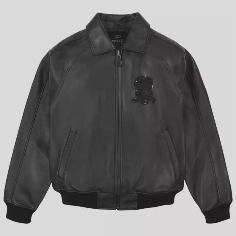 May include: Black leather bomber jacket with a zip-up front, collar, and two front pockets. The jacket features a black emblem on the chest and ribbed cuffs and hem. The jacket is a classic style.