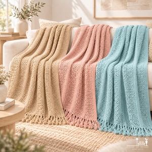 May include: Three knitted throw blankets in beige, dusty pink, and light blue, each featuring a vertical ribbed pattern with alternating textured knit sections and finished with knotted fringe edges, draped over a white sofa.