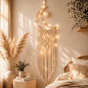 May include: A crescent moon-shaped macrame wall hanging made of off-white cord, featuring a central woven pattern, long fringe, and a small hanging moon charm. The piece is illuminated by warm white string lights woven throughout the structure.