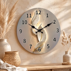 May include: A round wall clock with a beige face featuring two white, textured feather illustrations in the center. The clock has black Arabic numerals from 1 to 12 and black hour, minute, and second hands. The design includes subtle gold accents.