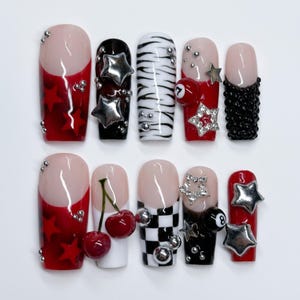 May include: A set of ten press-on nails featuring diverse designs including red and black colors, silver star charms, a 3D cherry motif, a black and white checkerboard pattern, zebra stripes, a billiard ball number 7 and 8, and small silver beads.