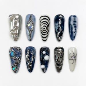 Könnte beinhalten: Ein Set aus zehn künstlichen Fingernägeln in Mandelform mit verschiedenen Designs, darunter metallisch silberne Texturen, schwarz-weiße Spiralen, dunkelblaue Marmormuster, irisierende Akzente und erhabene kugelförmige Verzierungen.