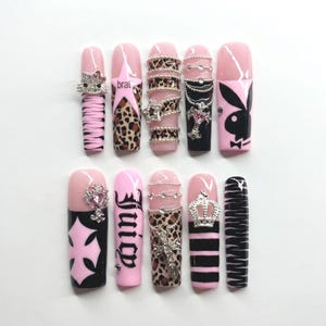 Puede incluir: Un conjunto de diez uñas postizas largas con varios diseños. Las uñas presentan patrones rosas, negros y de leopardo, junto con adornos como dijes, texto y un logotipo de Playboy. Algunas uñas tienen las palabras "brat" y "Juicy".