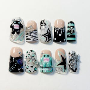 May include: A set of ten press-on nails featuring a variety of designs including black and white zebra stripes, leopard print, polka dots, and plaid. The nails are decorated with 3D monster charms, silver star accents, rhinestones, and fleur-de-lis.