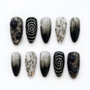 Könnte beinhalten: Ein Set aus zehn künstlichen Fingernägeln in einer monochromen Farbpalette aus Schwarz, Weiß und Grau. Die Designs umfassen marmorierte Rauchmuster, erhabene silberne Metallspiralen, flüssig wirkende Silberstrukturen und schwarze Kugeln.