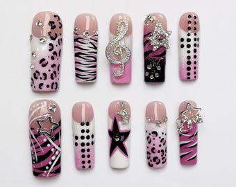 May include: A set of ten press-on nails featuring a pink, black, and white color palette. Designs include leopard print, zebra stripes, polka dots, and star patterns. Several nails are embellished with silver-toned charms, including a treble clef.
