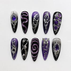 Può includere: Un set di dieci unghie finte lunghe a forma di mandorla. Ogni unghia presenta un design unico con accenti neri, viola e argento. I disegni includono vortici, gemme e abbellimenti metallici, creando un'estetica gotica o fantasy.