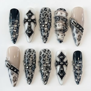 May include: A set of ten artificial nails in various designs. Some nails feature a black and white ombre effect, leopard print, or a beige base. Embellishments include silver studs, crosses, and metal accents.