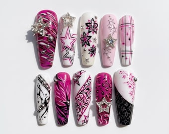 May include: A set of ten press-on nails featuring a variety of designs in pink, black, and white. The nails are decorated with star motifs, animal prints, tribal patterns, plaid lines, and silver-toned metallic studs and rhinestone star charms.