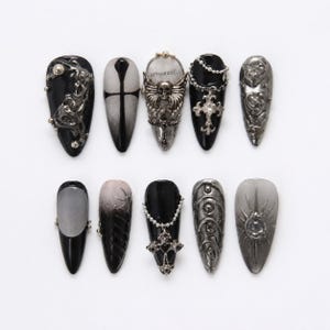 Könnte beinhalten: Ein Set von zehn künstlichen Nägeln im Gothic-Stil mit verschiedenen Designs. Die Nägel sind in Schwarz, Silber und Grau gehalten und mit Verzierungen wie Kreuzen, Totenköpfen und kunstvollen Metallarbeiten versehen. Einige Nägel haben einen Farbverlauf.