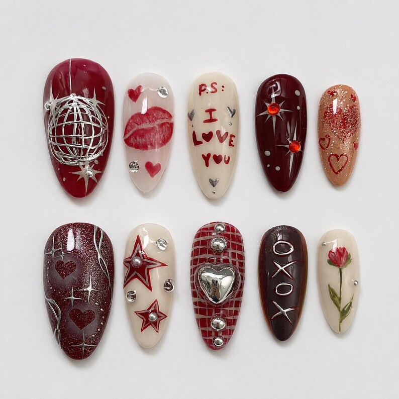 May include: A collection of ten artificial nails with diverse designs. The nails showcase colours like red, white, and brown. Designs include a globe, lips, hearts, stars, and the text "I Love You" and "XOXO".