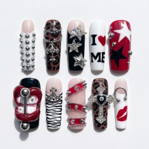 Könnte beinhalten: Eine Sammlung von zehn langen, Sarg-förmigen Press-on-Nägeln. Designs umfassen silberne Nieten, Leopardenmuster, Sternakzente, die Worte "I ❤️ ME", rote und schwarze Sterne, ein Lippenpiercing, Zebrastreifen, rote Nietenbänder, ein Kreuz und einen Lippenabdruck.