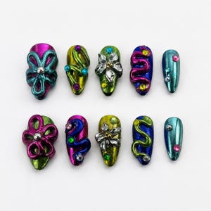 Könnte beinhalten: Ein Set aus zehn künstlichen Fingernägeln mit metallischem Finish in Magenta, Limettengrün, Blau und Türkis. Die Designs umfassen erhabene 3D-Blumenformen, geschwungene Linien und kleine, auf jeder Nageloberfläche eingebettete Strasssteine.