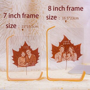 May include: Two clear acrylic photo frames with wooden stands. Each frame features a family portrait etched onto a maple leaf design. The 7-inch frame measures 15 x 19.5 cm, and the 8-inch frame is 16.5 x 23 cm. Text on the frames reads.