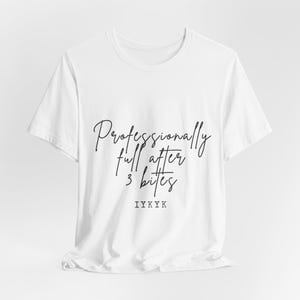 Könnte beinhalten: Weißes T-Shirt mit dem Text "Professionell satt nach 3 Bissen" in schwarzer Schrift. Der Satz "IYKYK" ist darunter gedruckt. Das Shirt besteht aus einem weichen, leichten Material.