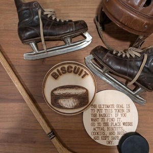 May include: A pair of vintage brown leather ice skates, a brown leather hockey helmet, a wooden hockey stick, a black hockey puck, and two circular wooden plaques. One plaque features a hockey puck and the word BISCUIT, while the other has text.