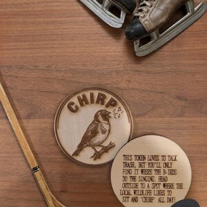 May include: Two circular wooden tokens with laser-engraved designs. One token features a bird on a branch with the text CHIRP. The other token displays the text: THIS TOKEN LOVES TO TALK TRASH, BUT YOU'LL ONLY FIND IT WHERE THE B-IRDS DO THE SINGING.