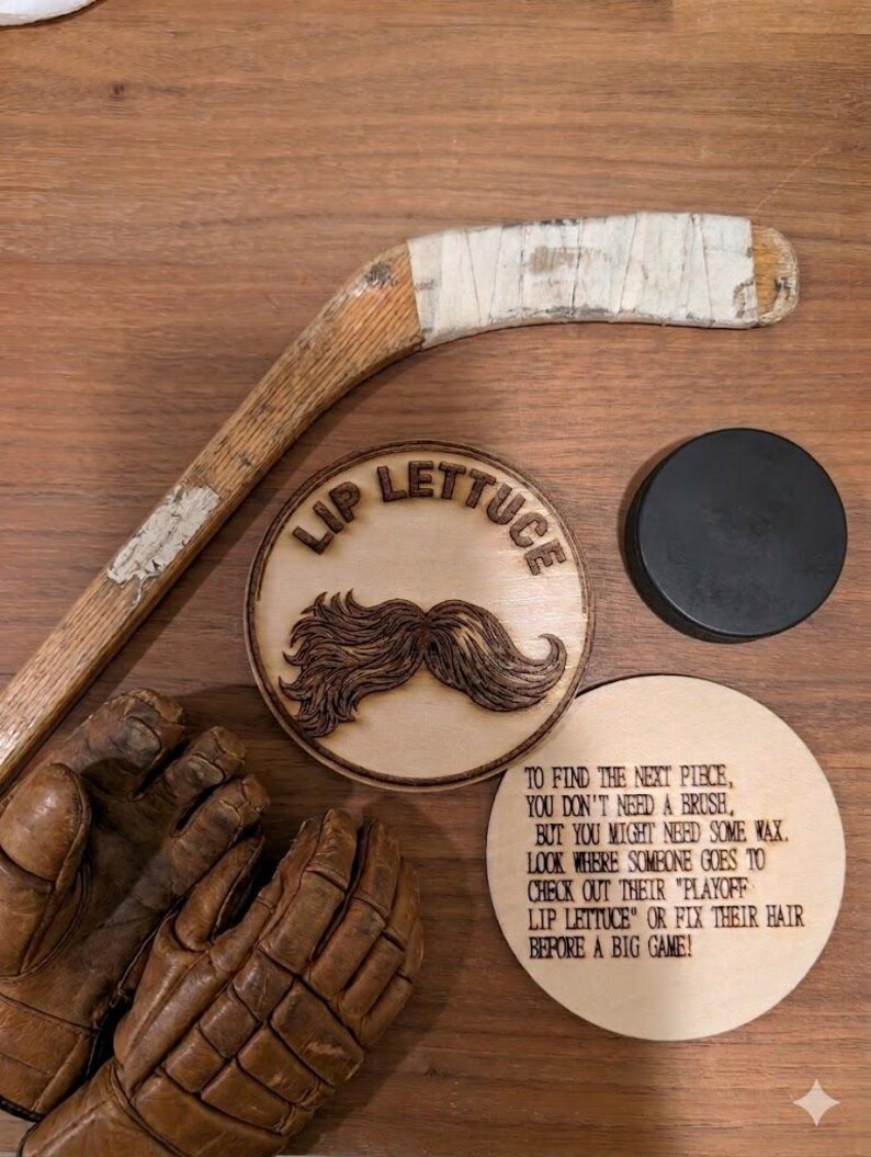 May include: A wooden hockey stick with white tape, a pair of brown leather hockey gloves, a black hockey puck, and two circular wooden plaques. One plaque features a wood-burned moustache and the text "LIP LETTUCE," while the other contains a printed riddle.
