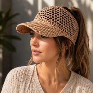 May include: A beige crochet visor hat featuring an open hexagonal mesh pattern on the crown and a solid, tightly woven brim. The visor is constructed from a textured, yarn-like material in a neutral tan color, designed with an open back style.
